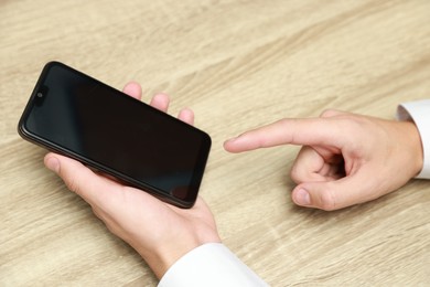 Photo of Man using smartphone with blank screen at wooden table, closeup