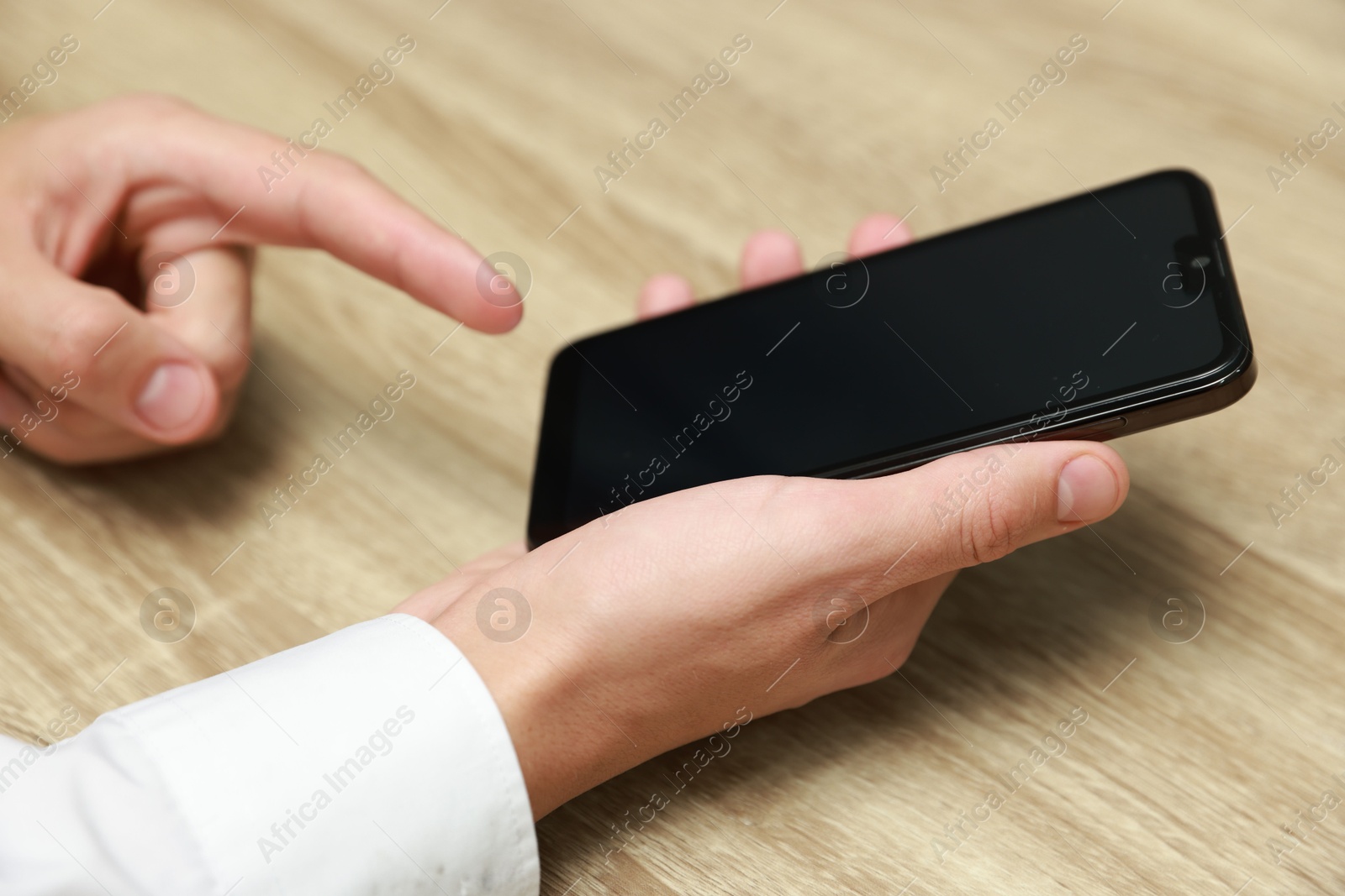 Photo of Man using smartphone with blank screen at wooden table, closeup