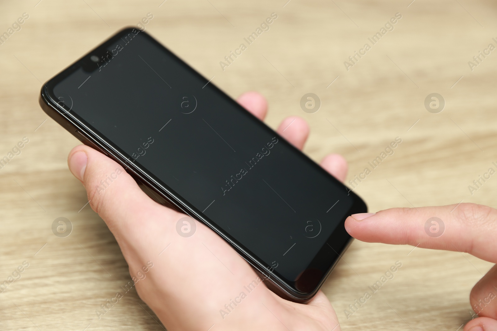 Photo of Man using smartphone with blank screen at wooden table, closeup