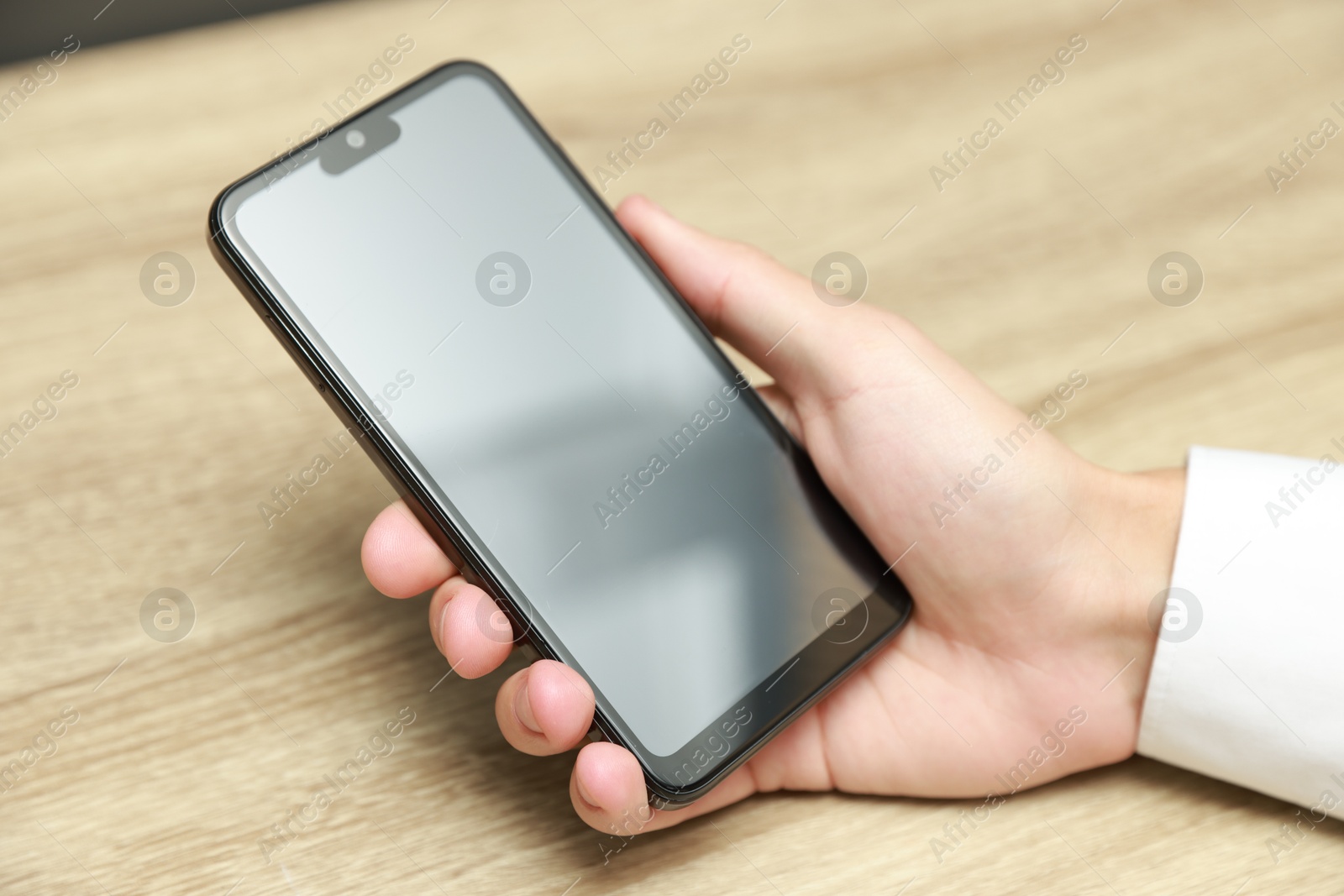 Photo of Man using smartphone with blank screen at wooden table, closeup