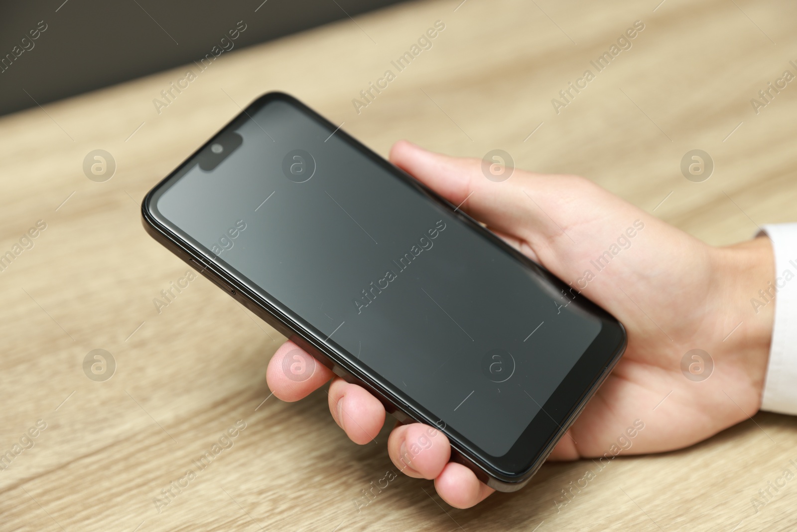 Photo of Man using smartphone with blank screen at wooden table, closeup