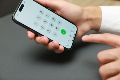 Photo of Man dialing number on smartphone at grey table, closeup