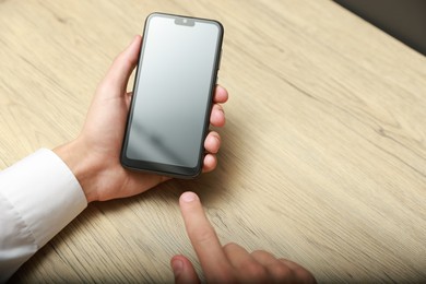 Photo of Man using smartphone with blank screen at wooden table, closeup. Space for text