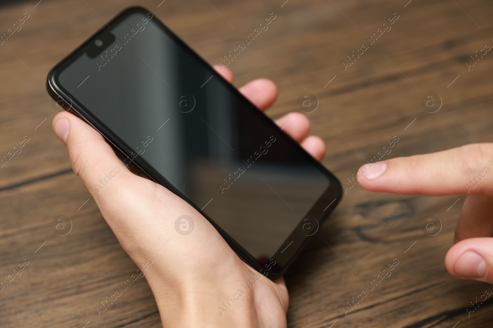 Photo of Man using smartphone with blank screen at wooden table, closeup