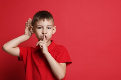 Photo of Little boy showing hand to ear gesture on red background, space for text