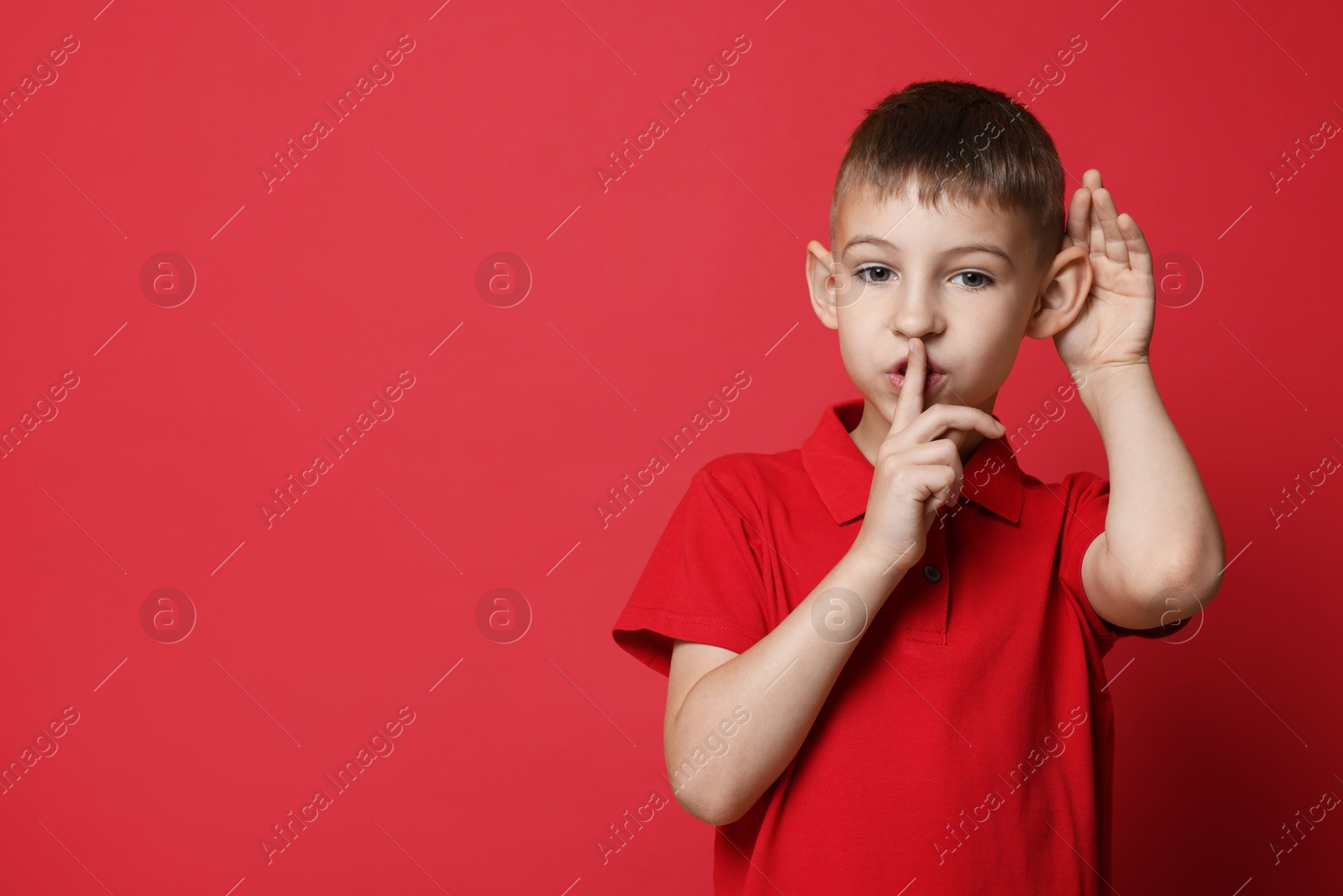 Photo of Little boy showing hand to ear gesture on red background, space for text