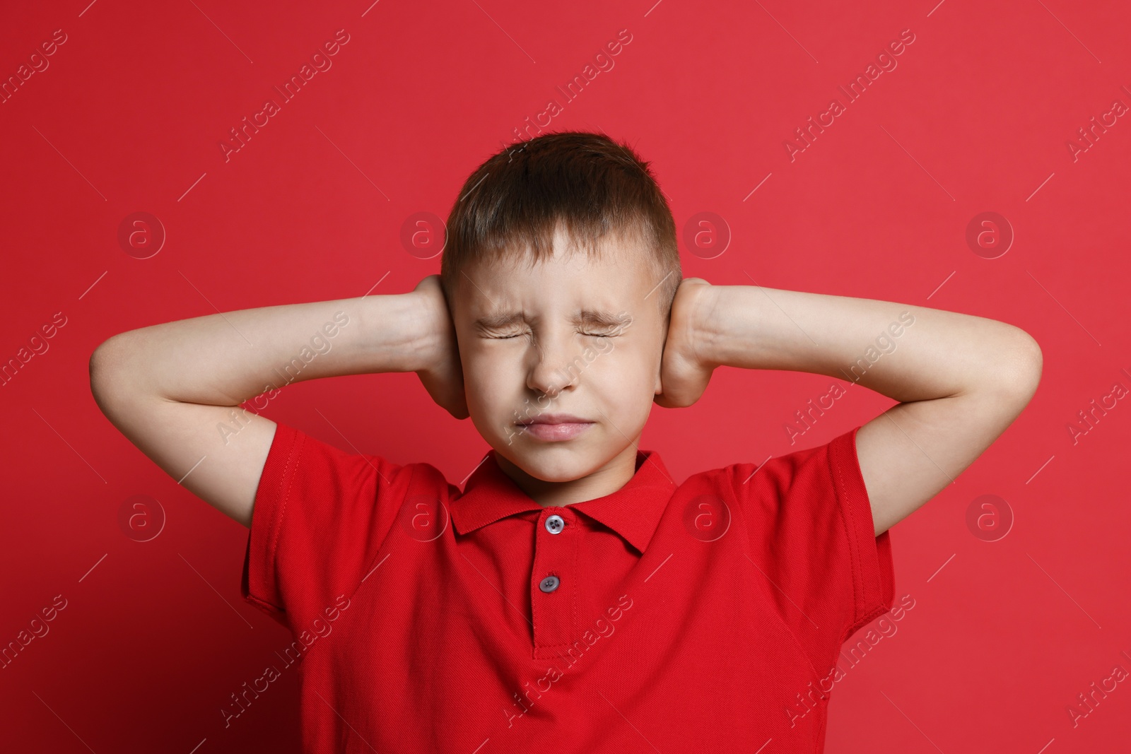 Photo of Little boy covering his ears on red background