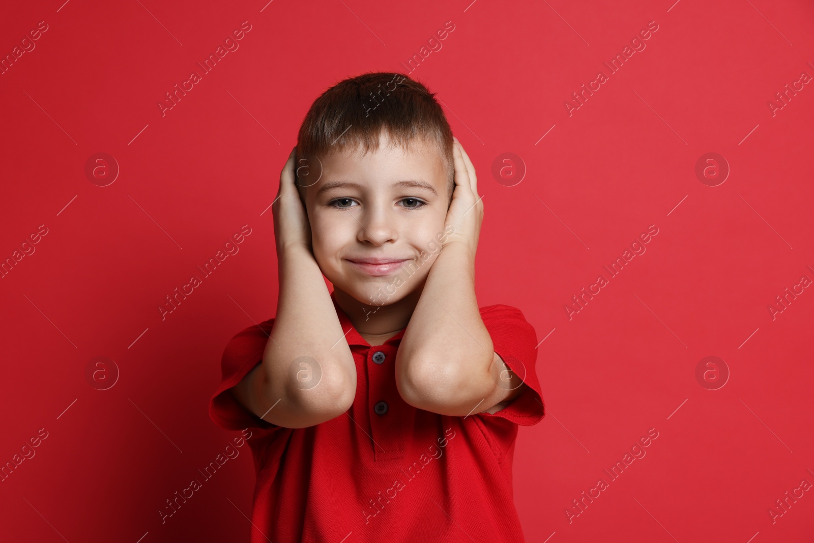 Photo of Little boy covering his ears on red background