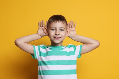 Photo of Little boy showing hand to ear gesture on orange background