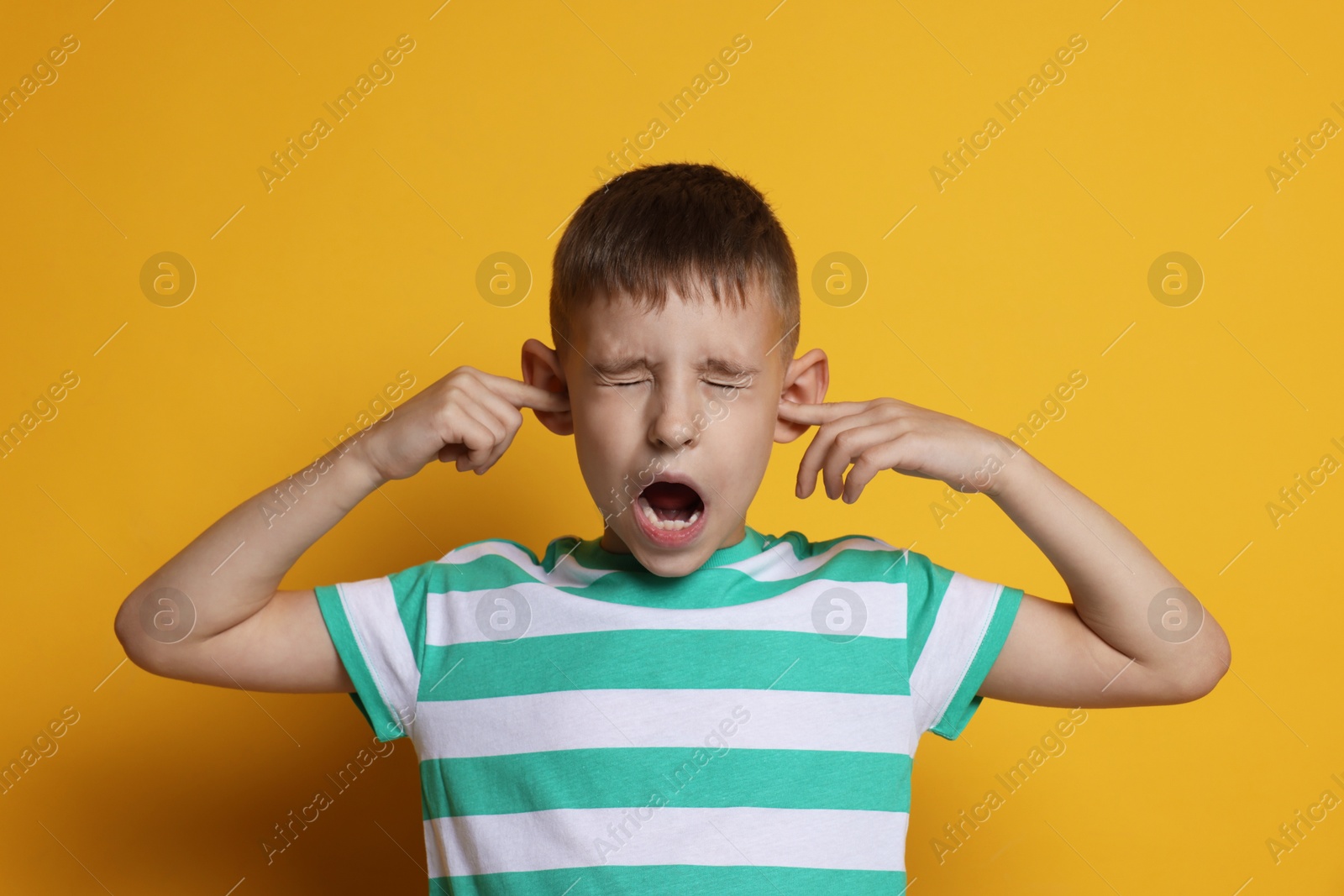 Photo of Little boy covering his ears with fingers on orange background