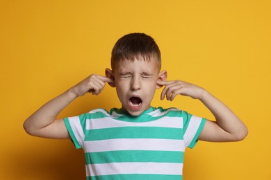 Little boy covering his ears with fingers on orange background