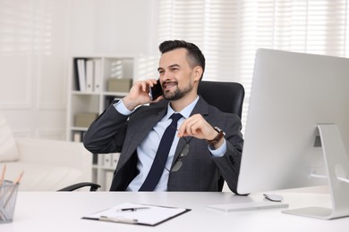 Photo of Happy banker talking on smartphone at table in office