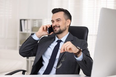 Photo of Happy banker talking on smartphone at table in office