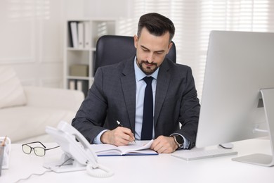 Photo of Handsome banker making notes at table in office