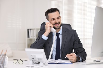 Photo of Happy banker talking on phone at table in office