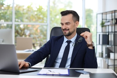 Photo of Happy banker working with laptop at table in office