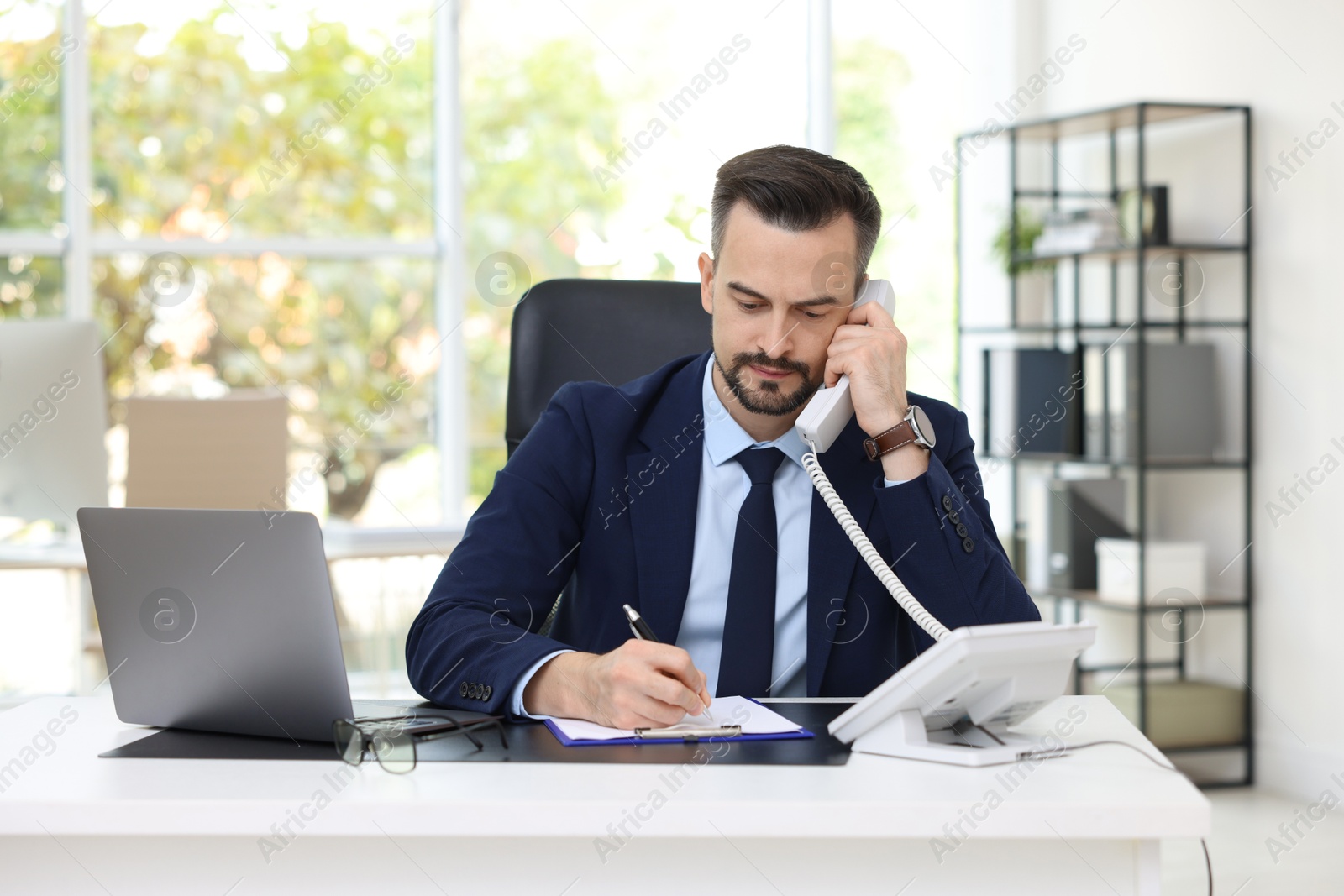 Photo of Handsome banker talking on phone at table in office