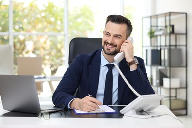 Photo of Happy banker talking on phone at table in office