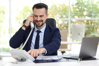 Photo of Happy banker talking on phone at table in office