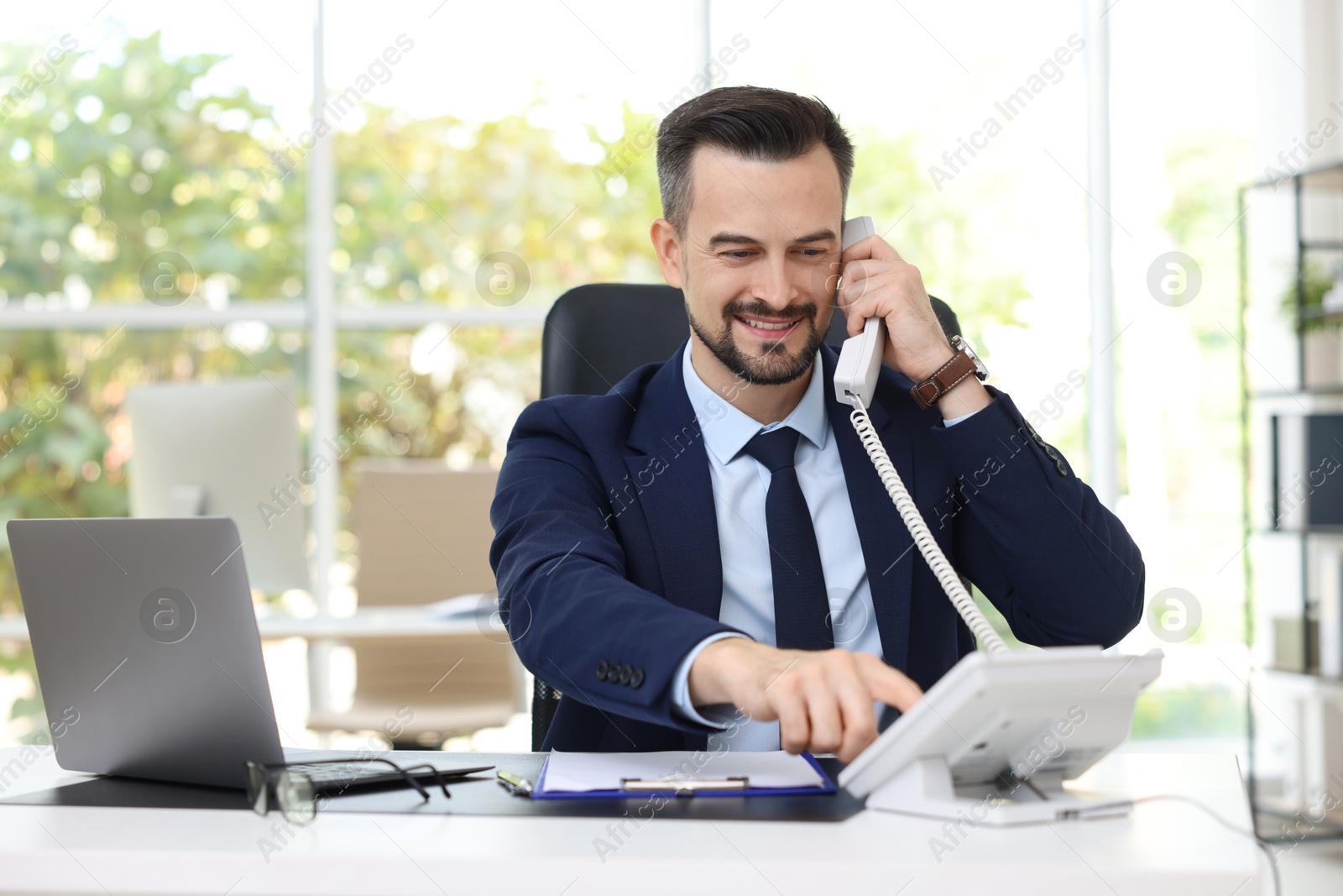 Photo of Happy banker talking on phone at table in office