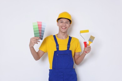 Photo of Portrait of young decorator with paint roller, color palettes and brush on white background