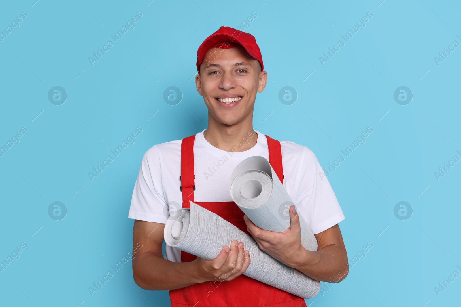 Photo of Young decorator with rolls of wallpaper on light blue background