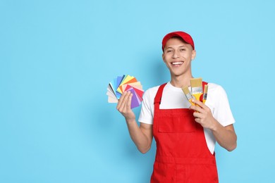 Photo of Portrait of young decorator with color palettes and brushes on light blue background, space for text