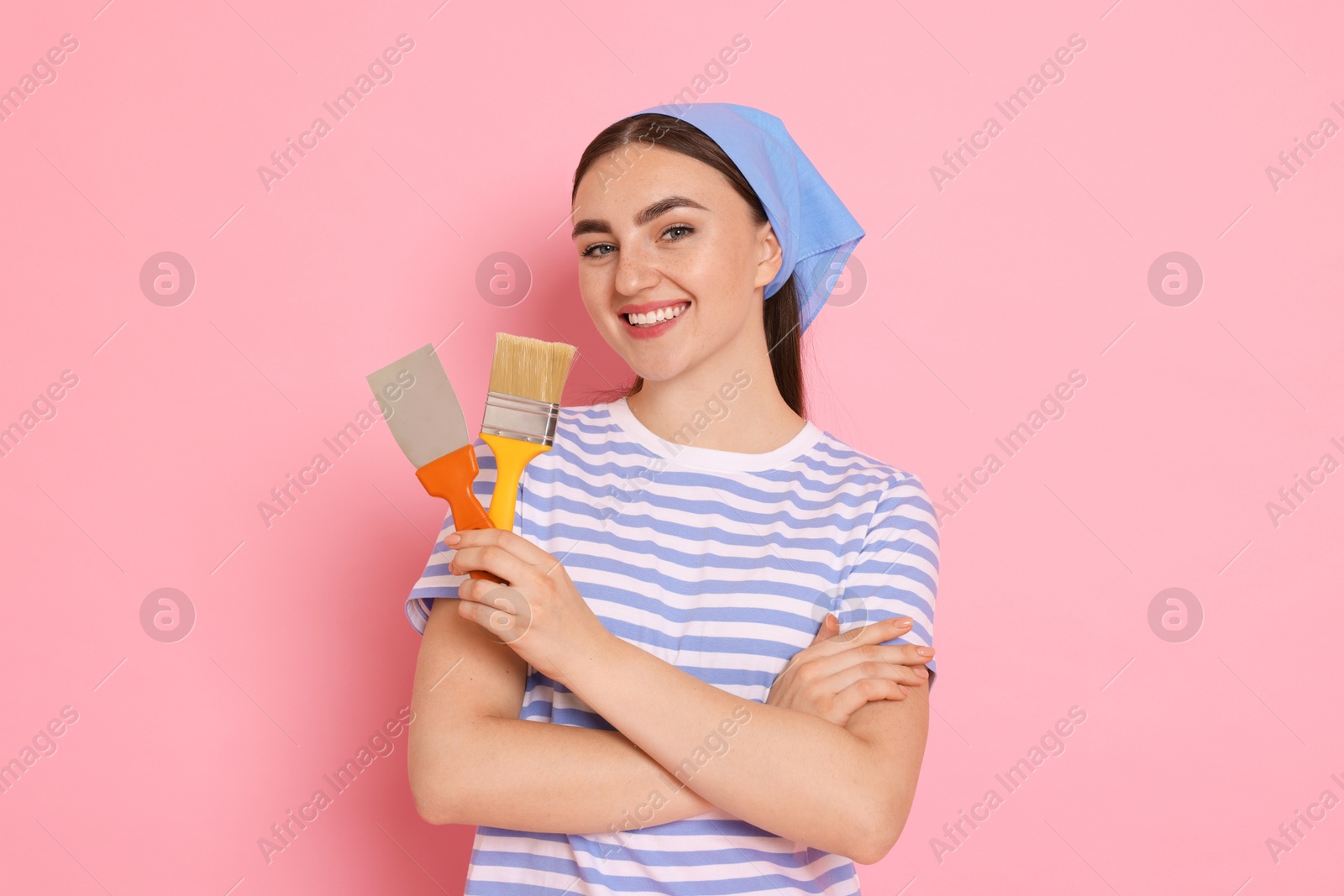 Photo of Portrait of young decorator with putty knife and brush on pink background