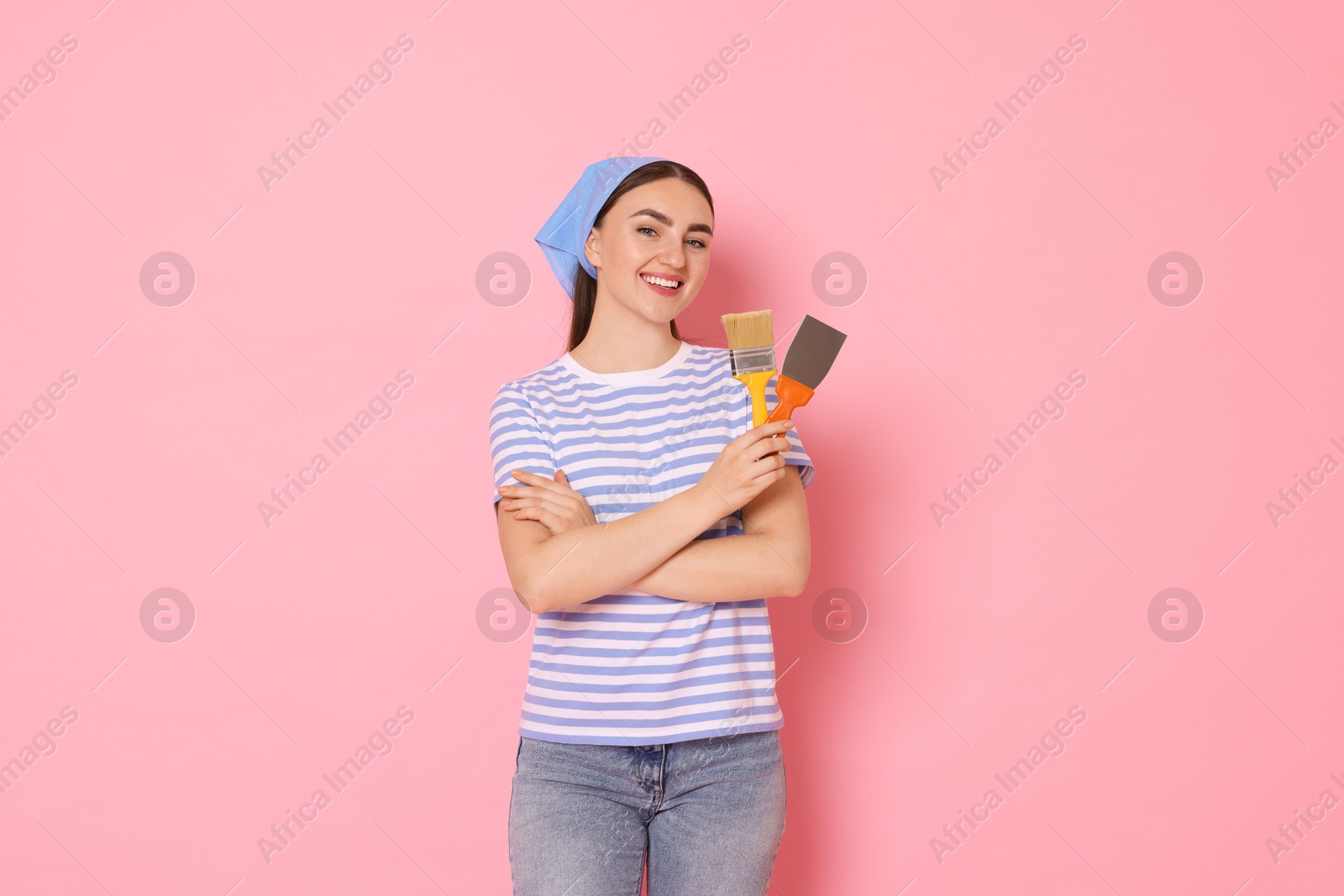 Photo of Portrait of young decorator with putty knife and brush on pink background