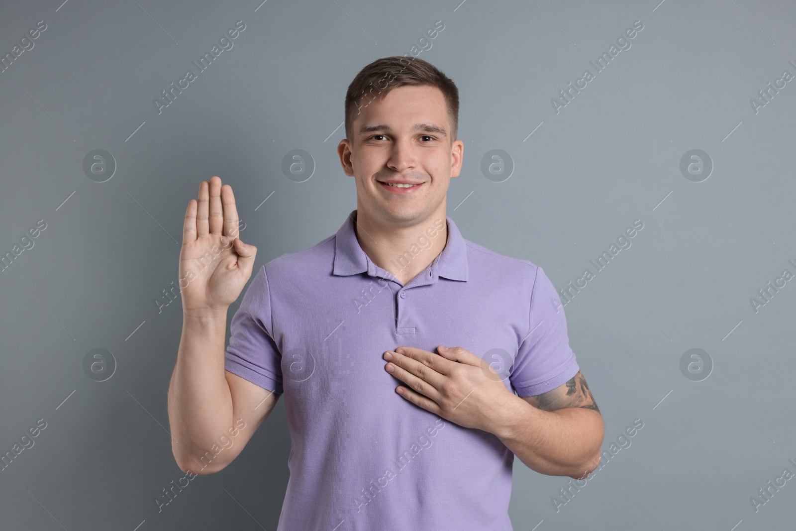 Photo of Man making promise with raised hand on grey background. Oath gesture