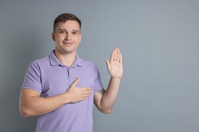 Photo of Man making promise with raised hand on grey background, space for text. Oath gesture