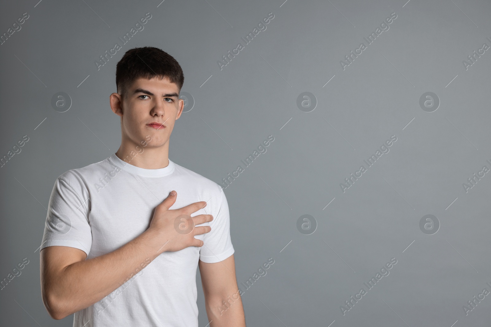 Photo of Man making promise on grey background, space for text. Oath gesture