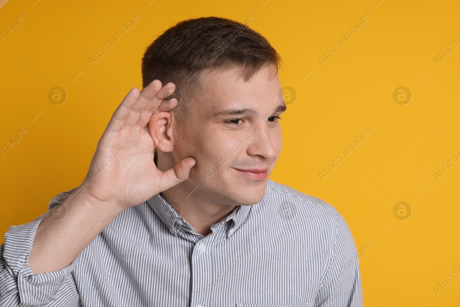 Photo of Man showing hand to ear gesture on orange background