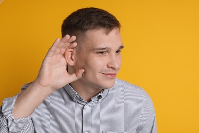 Photo of Man showing hand to ear gesture on orange background