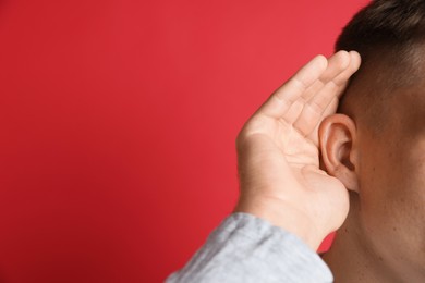 Photo of Man showing hand to ear gesture on red background, closeup. Space for text