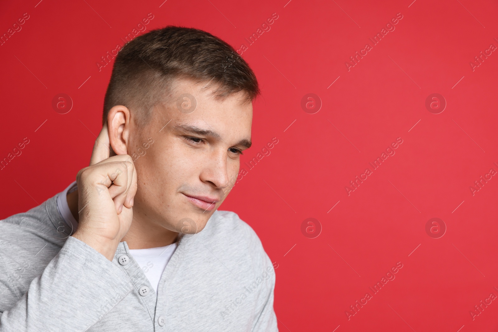 Photo of Man showing hand to ear gesture on red background, space for text