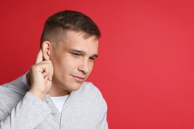 Photo of Man showing hand to ear gesture on red background, space for text