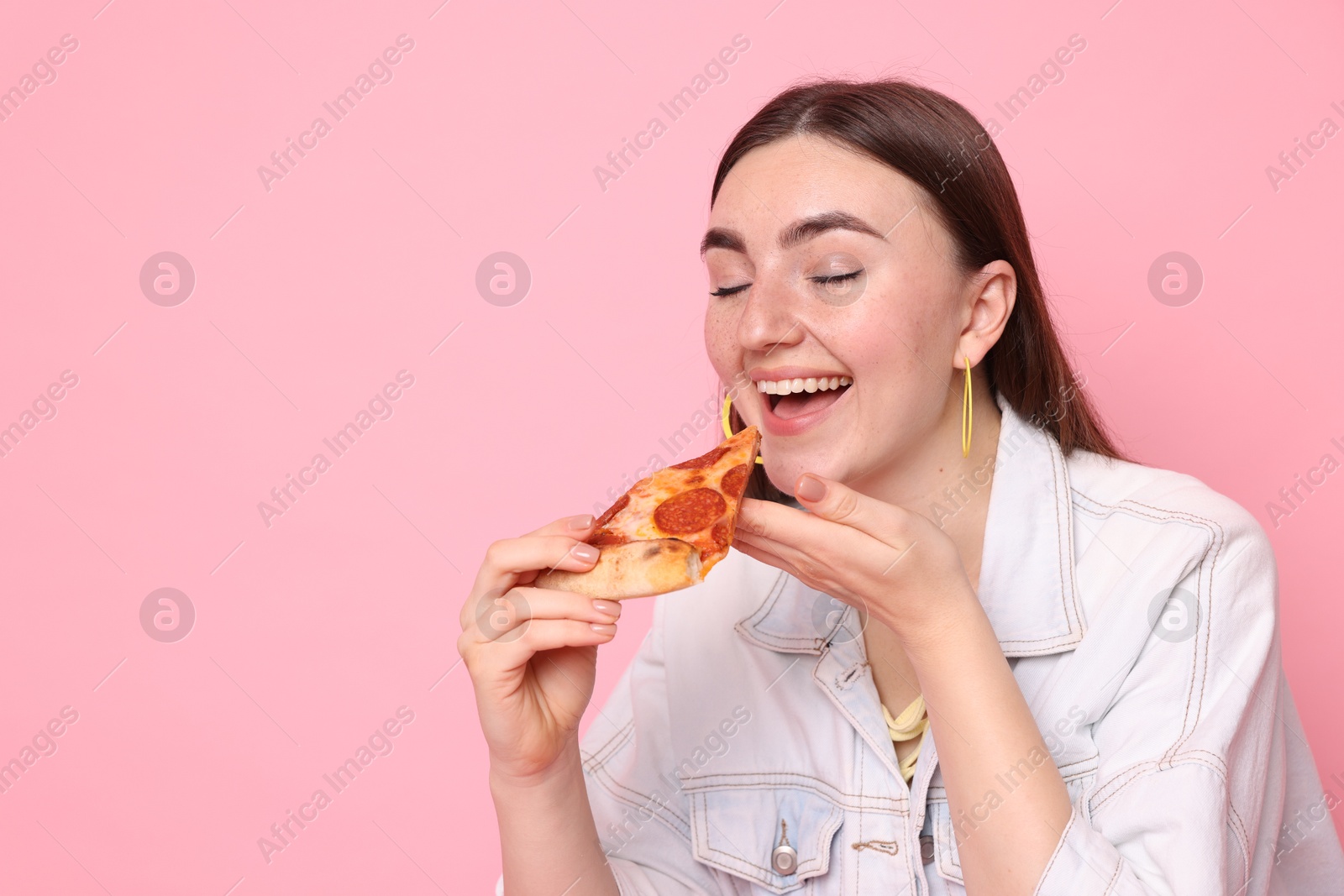 Photo of Beautiful woman eating pizza on pink background, space for text