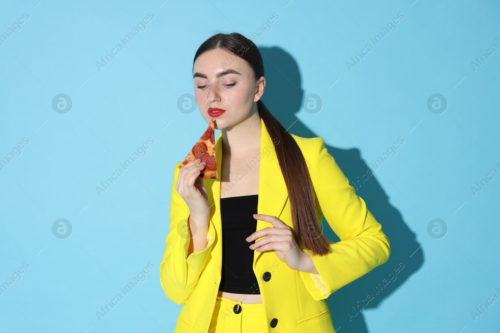 Photo of Beautiful woman with piece of pizza on light blue background