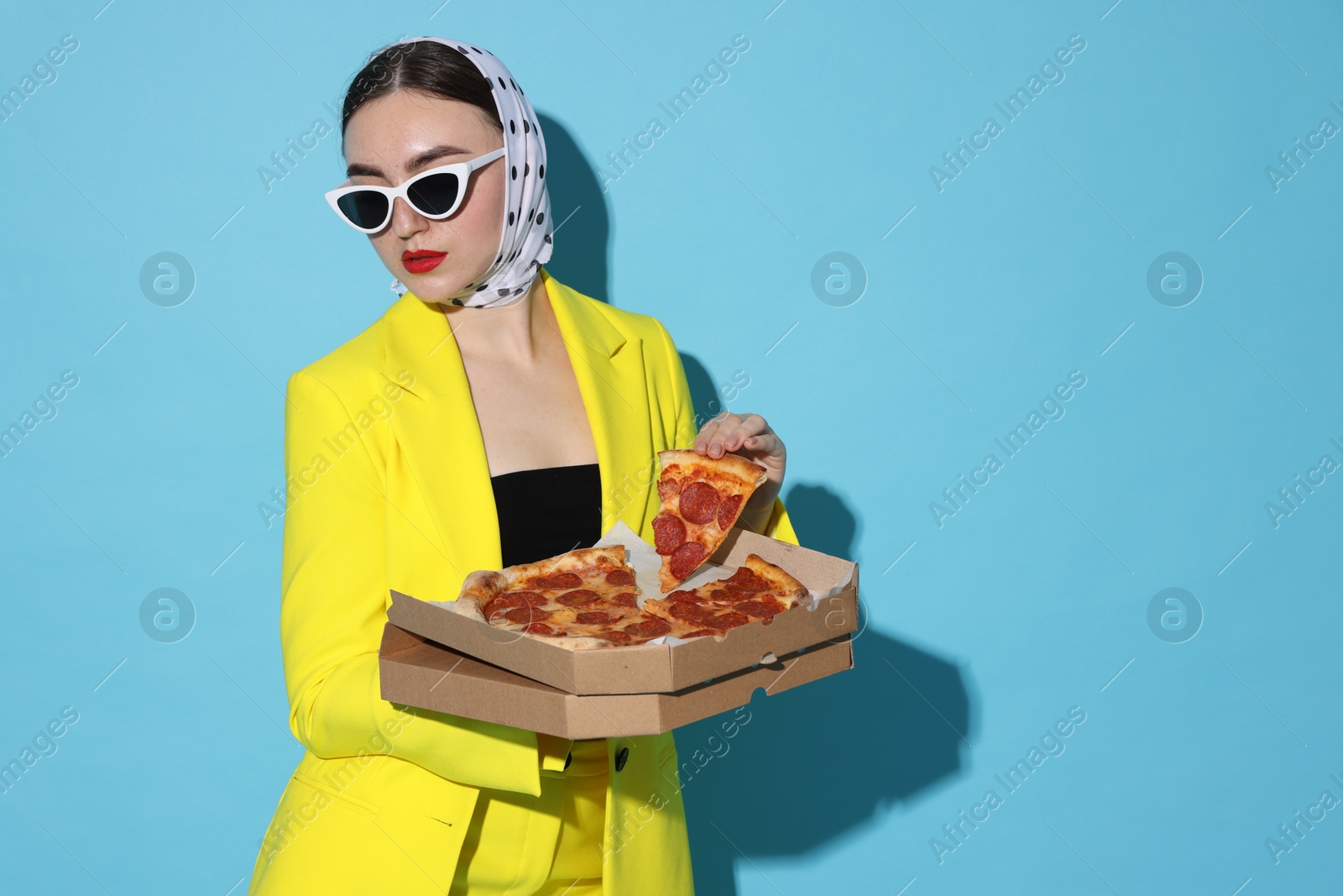 Photo of Stylish woman with delicious pizza on light blue background, space for text