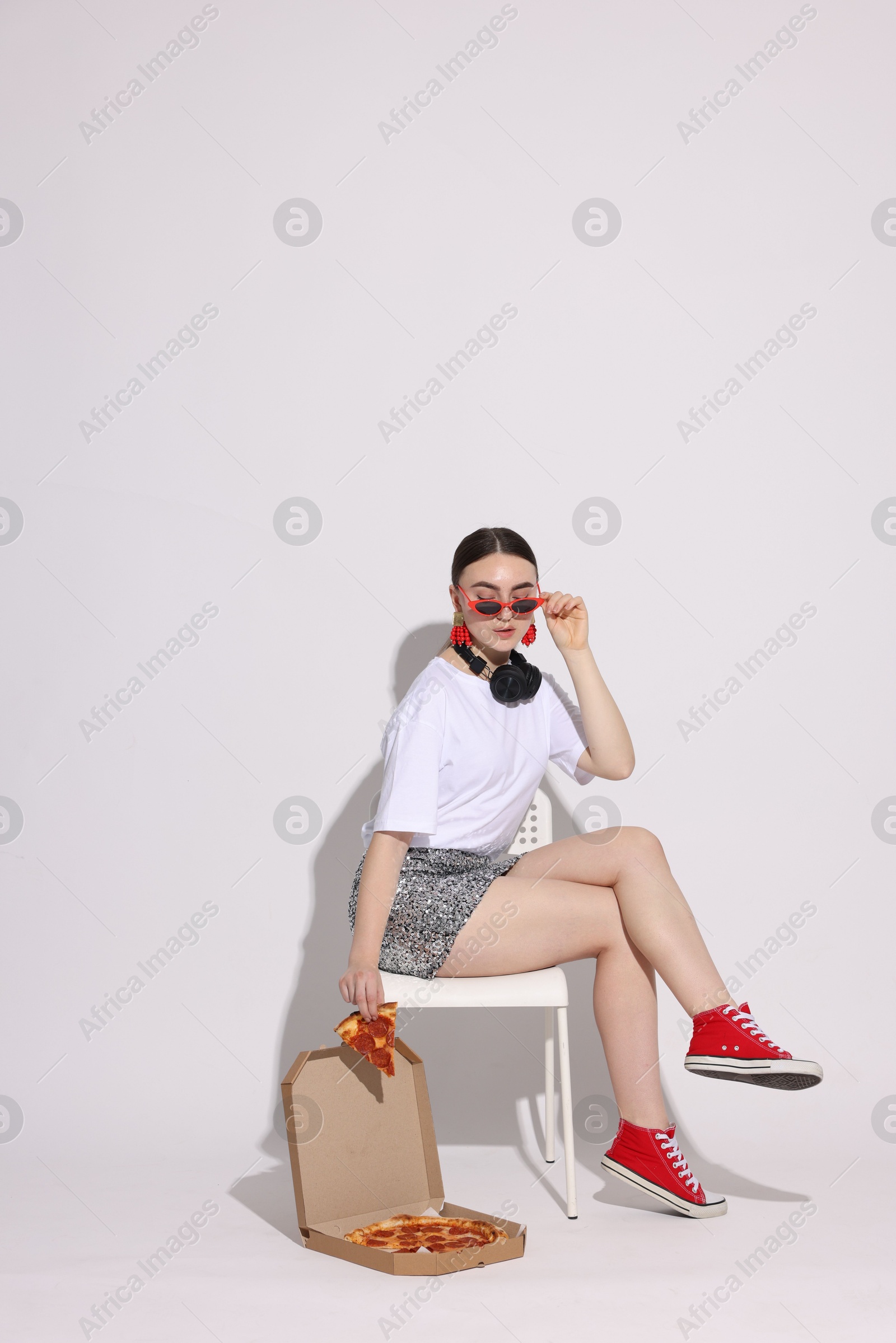 Photo of Woman in sunglasses with delicious pizza sitting on chair against white background, space for text