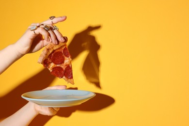 Photo of Woman with piece of delicious pizza on orange background, closeup. Space for text