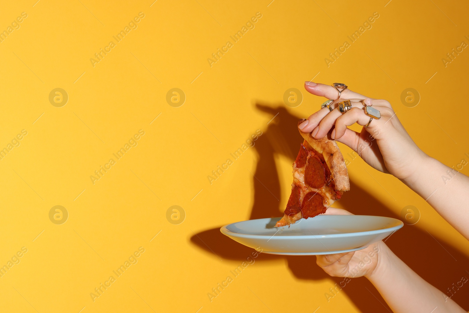 Photo of Woman with piece of delicious pizza on orange background, closeup. Space for text