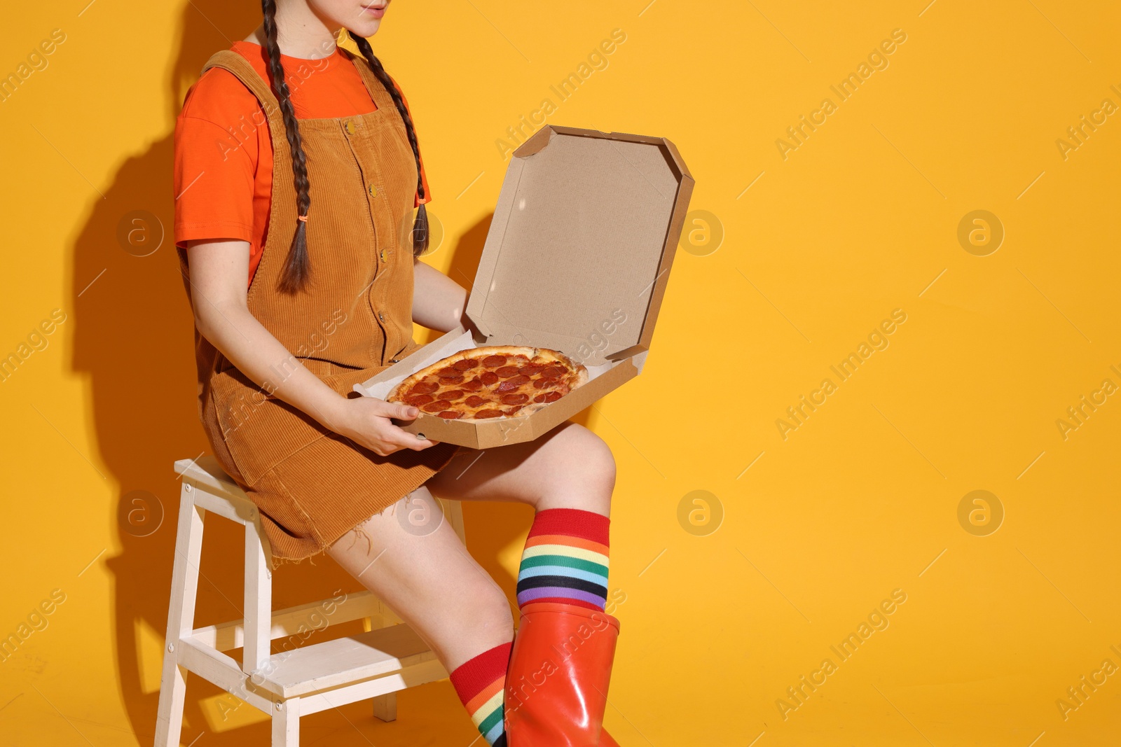 Photo of Woman with delicious pizza sitting on step stool against orange background, closeup. Space for text