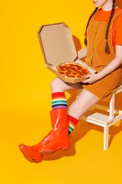 Photo of Woman with delicious pizza sitting on step stool against orange background, closeup