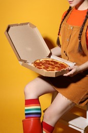 Woman with delicious pizza sitting on step stool against orange background, closeup