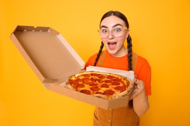 Surprised woman with delicious pizza on orange background