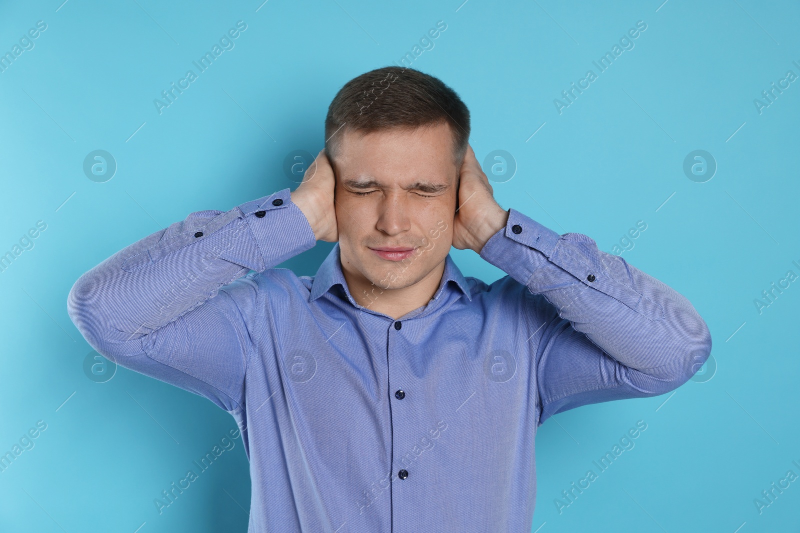 Photo of Man covering his ears on light blue background