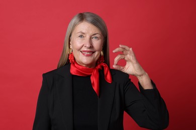 Senior woman showing okay gesture on red background