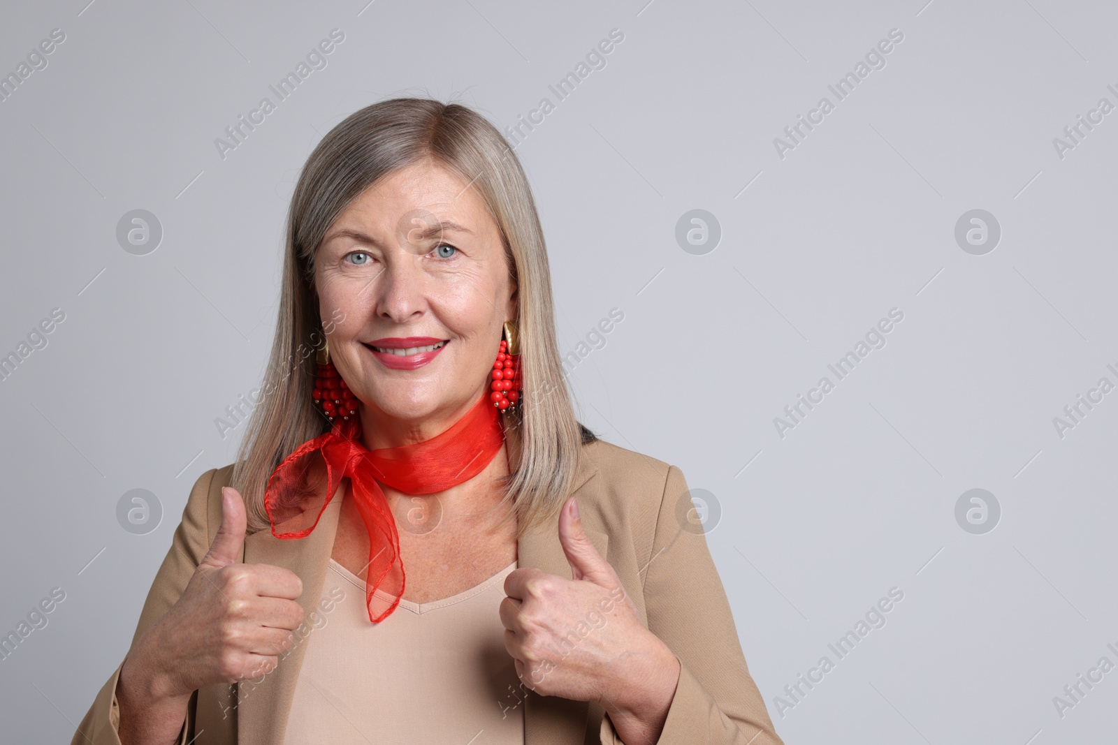 Photo of Senior woman showing thumbs up on light grey background. Space for text